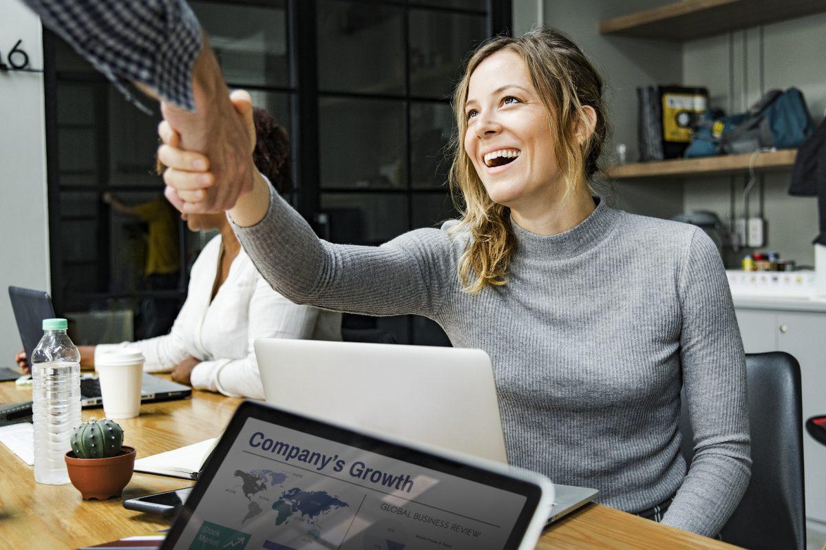 Woman shaking hands with man in agreement with words "company growth" in a laptop