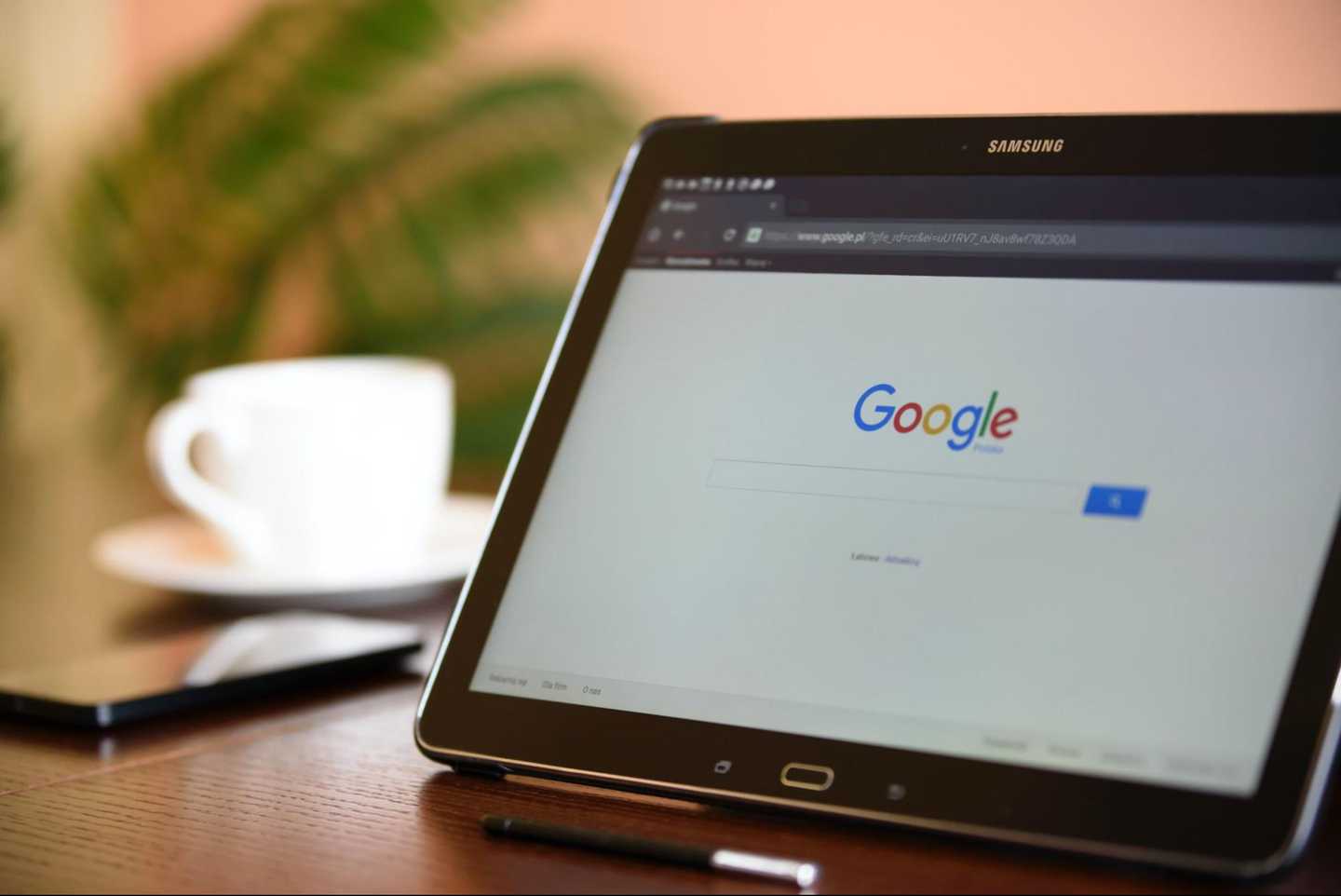 Google homepage in ipad screen and a phone and coffee mug beside