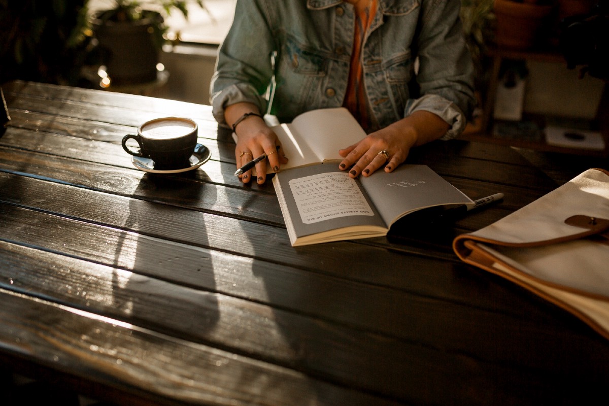 A girl writing ina notebook with a cup of coffee beside