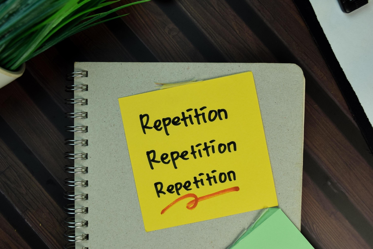 Repetition written 3 times on a yellow sticky note on a notebook