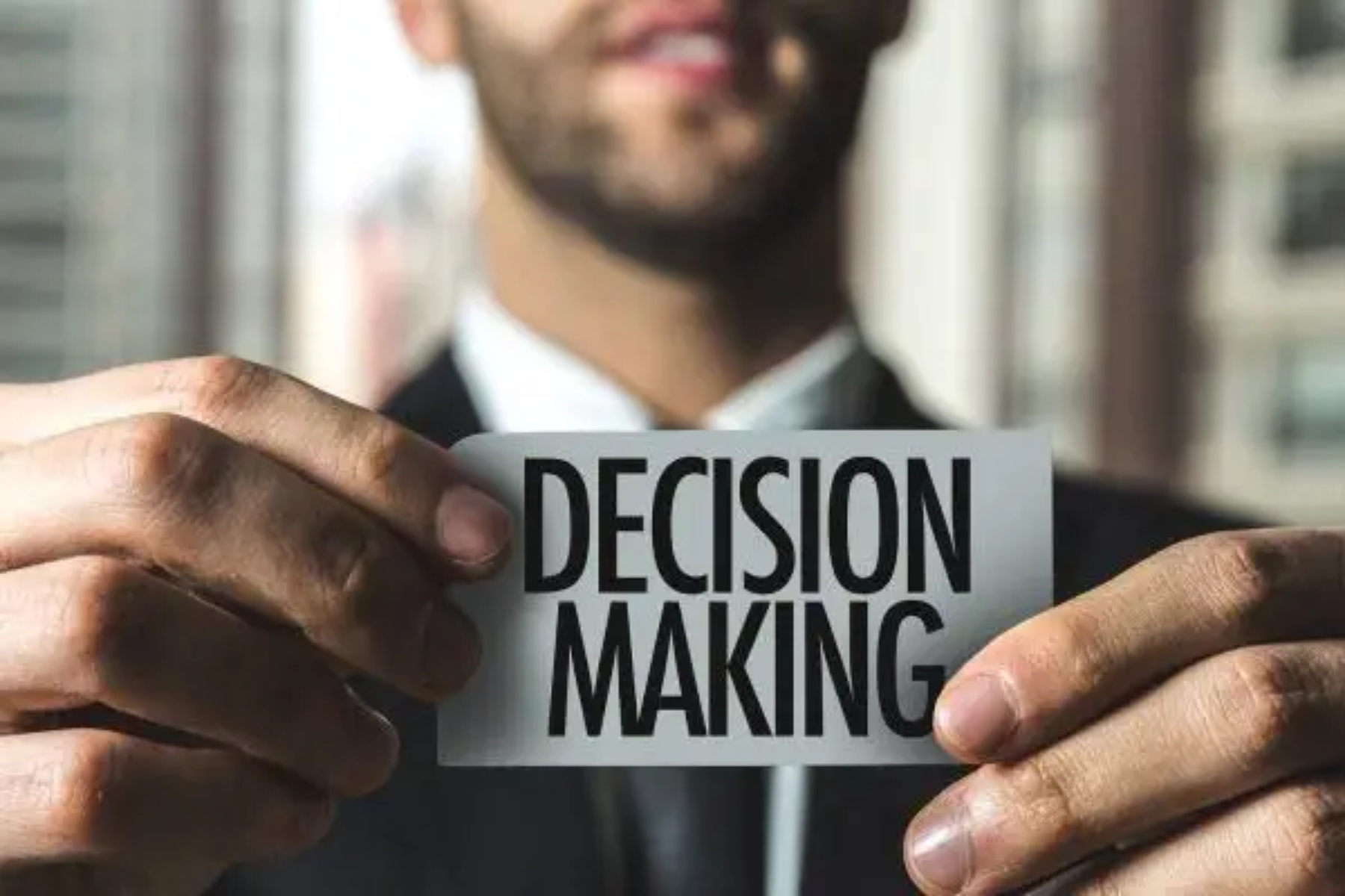 In front of the camera, a businessman holds a piece of paper with the words "Decision Making"