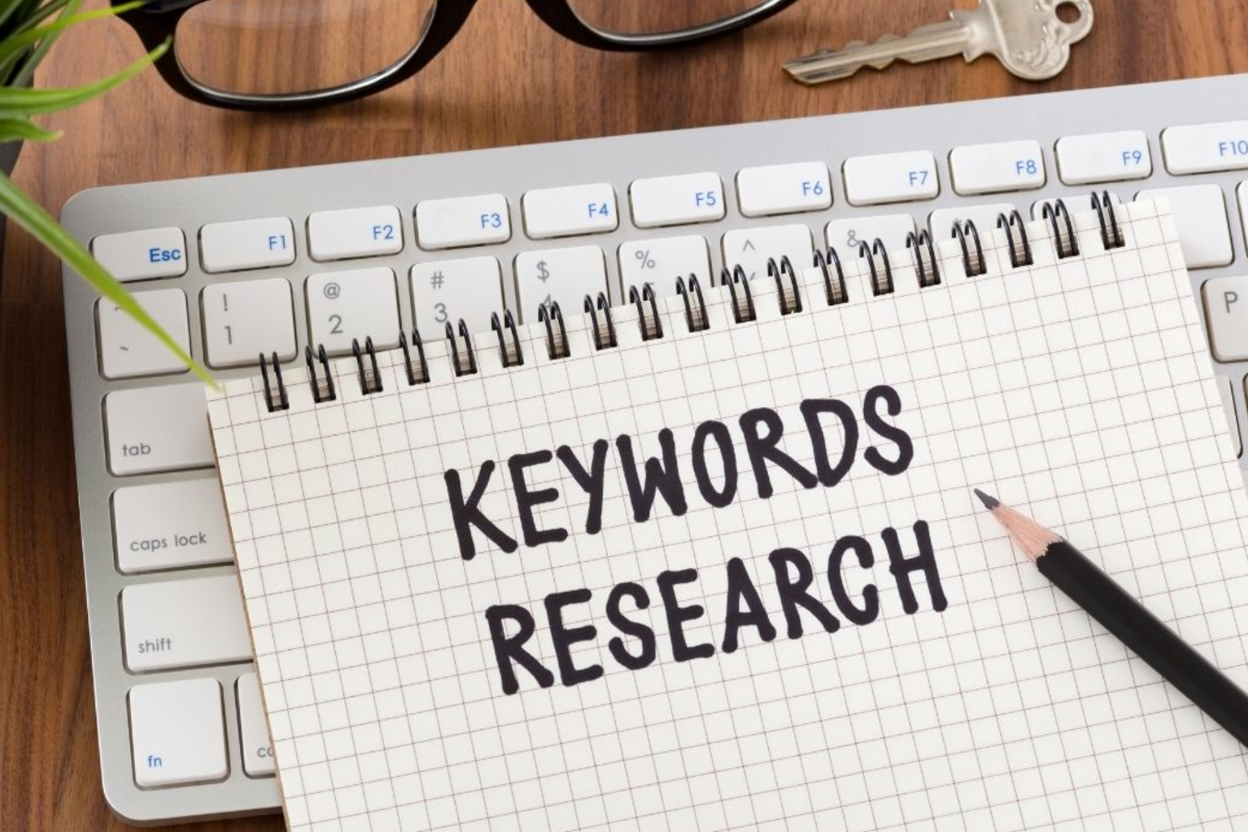 A notebook with the words "Keywords Research" written on it sits on top of the keyboard