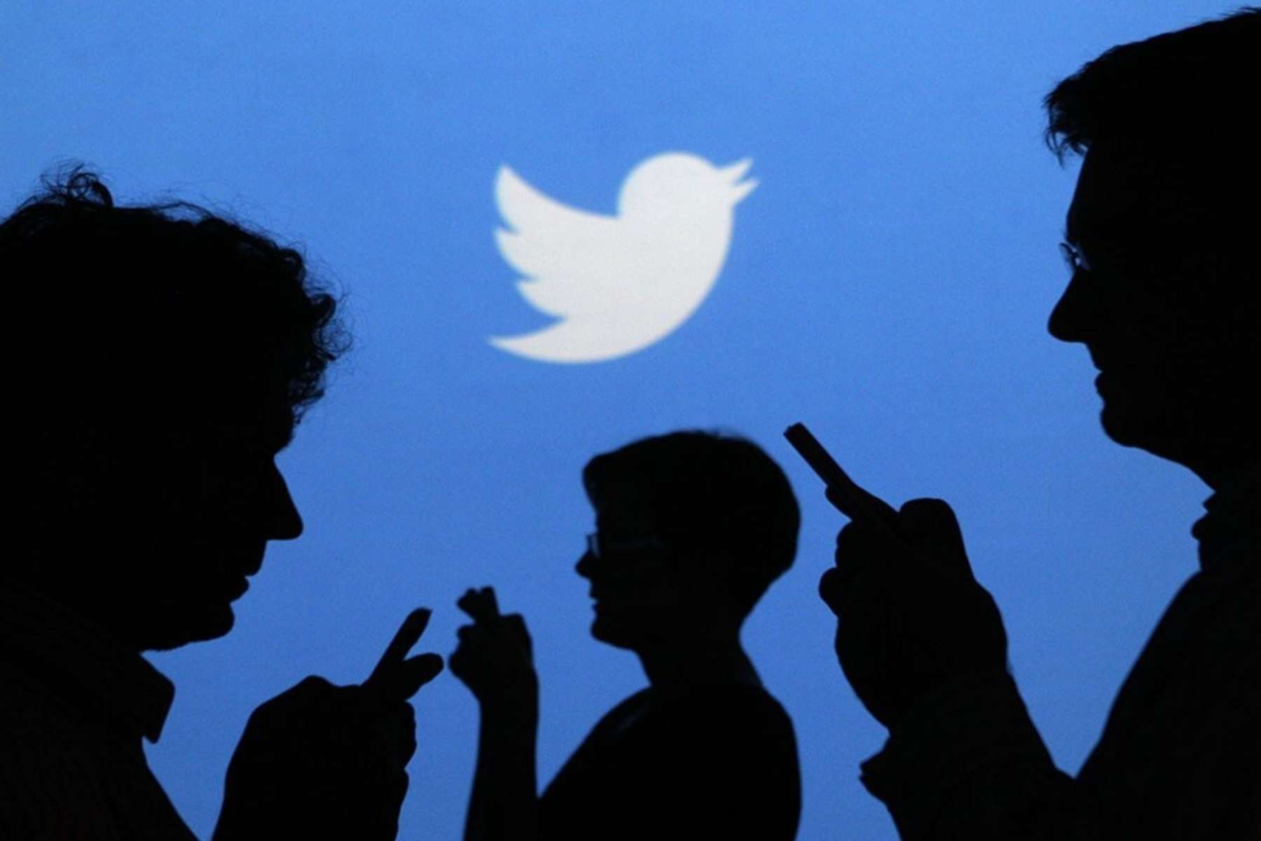 A silhouette of individuals using mobile devices with the Twitter logo