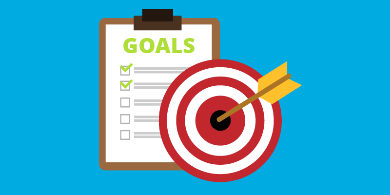 A piece of paper with the word "Goals" and checkboxes placed next to a dartboard