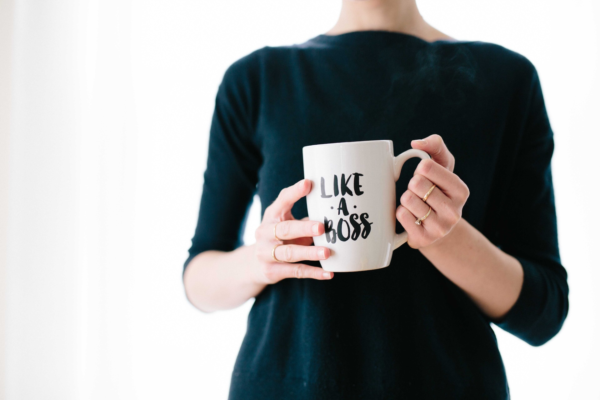 A headless woman in black clothes holding with both hands a white mug with the words ‘like a boss’ in black