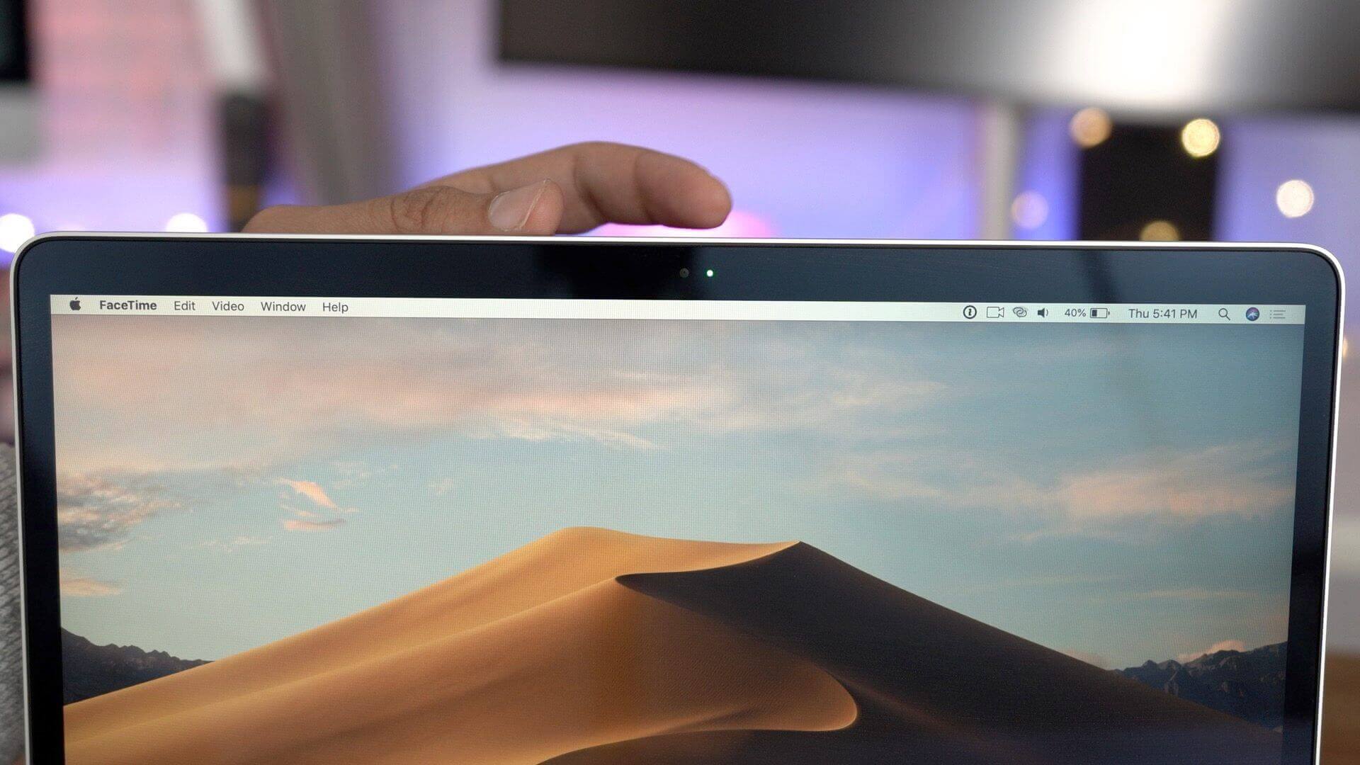 A macbook showing a desert on screen with a hand on the back of the screen