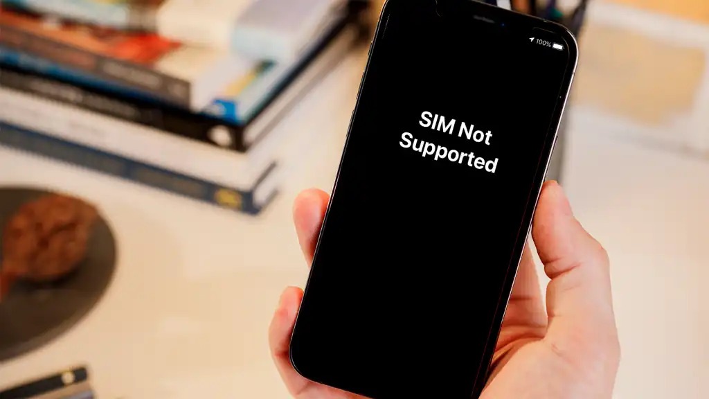 Hand holding a black iphone with SIM not supported written on screen