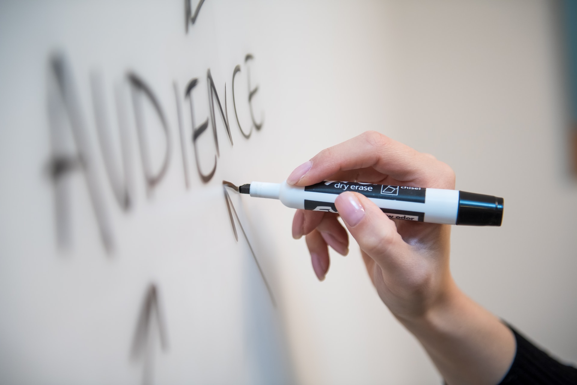 A woman’s hand drawing on a whiteboard an arrow pointed at the word ‘audience’ in uppercase letters