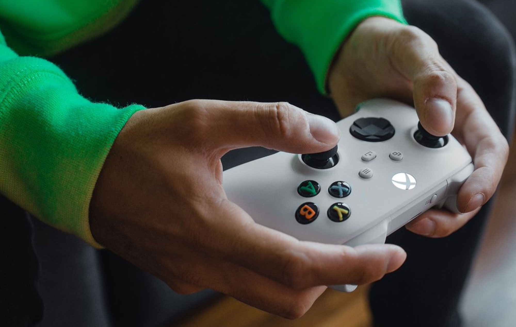 Hand wearing green sleeves holding a white xbox controller