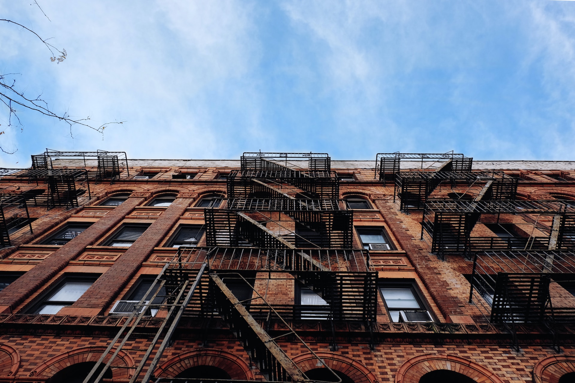 A view from the ground of a red brick apartment in New York, with iron fire escapes and the blue sky