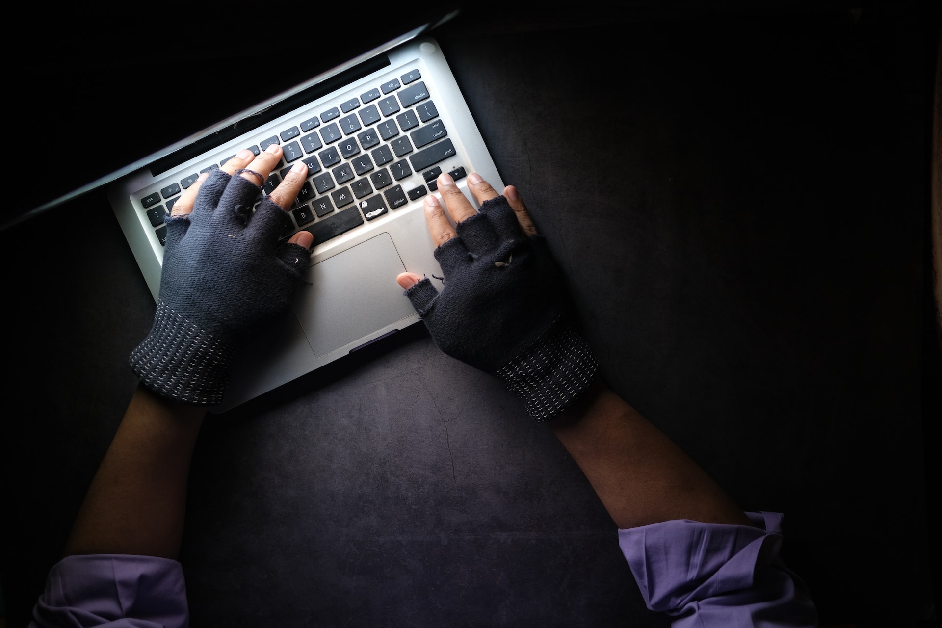 Hands with black gloves typing on a laptop
