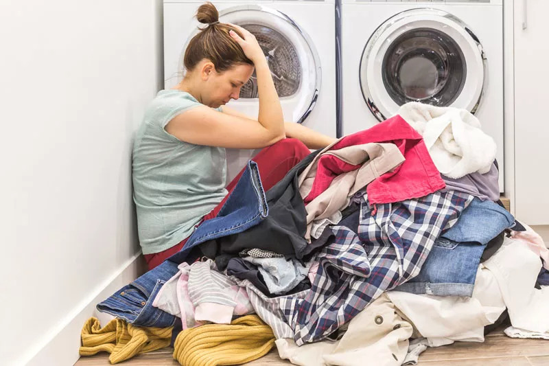 Frustrated woman on the floor surrounded with clothes beside a washer and dryer