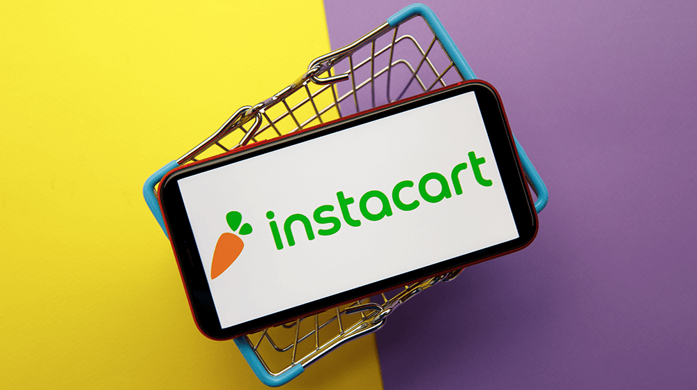 A phone with the instacart logo on screen on a small basket.