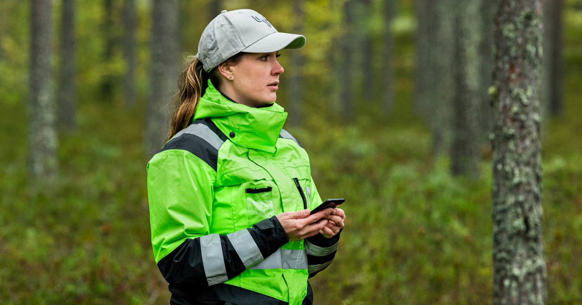 A woman in a green jacket and gray cap on a forest