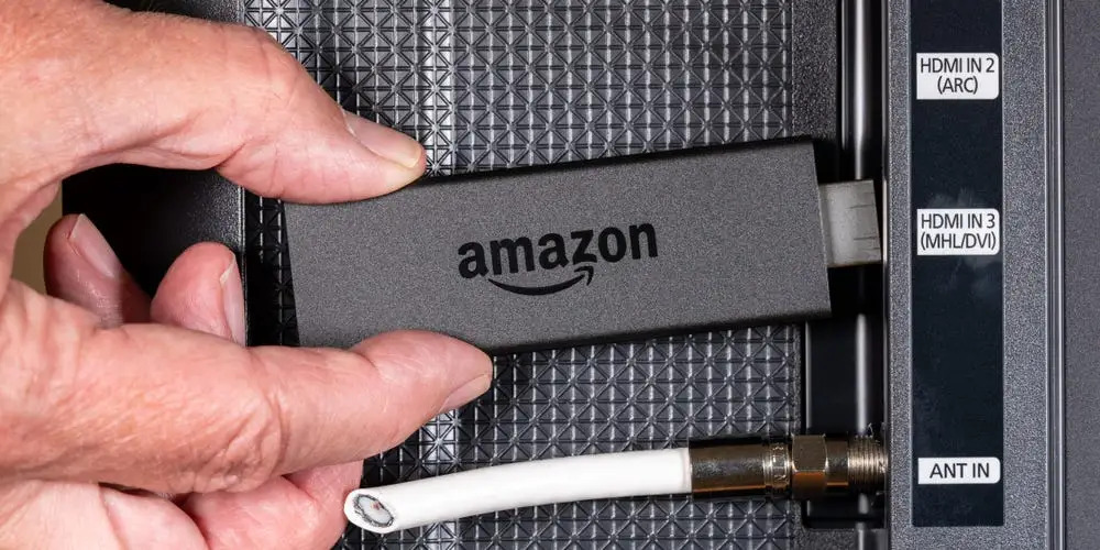 A hand holding an Amazon Fire TV Stick to an HDMI port. 