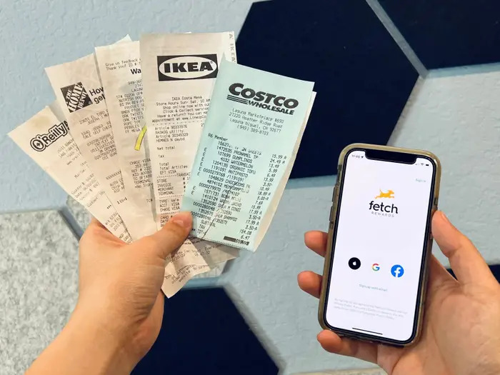 A person's hand holding a fan of receipts on one hand and a phone with Fetch Rewards App opened on the other.