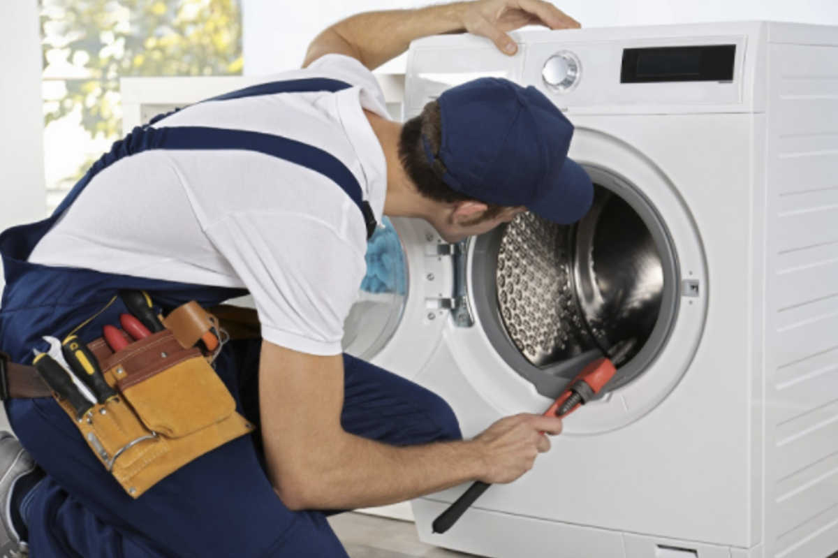 A man in blue jumpsuit fixing a washer