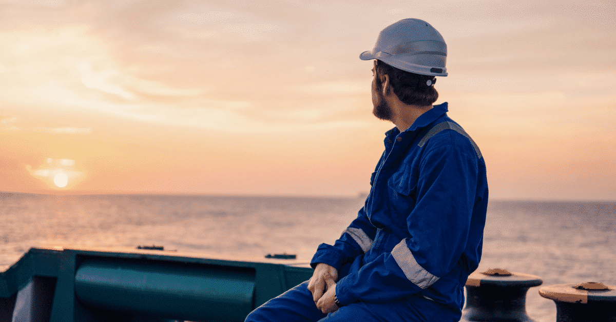 A man in blue jumpsuit looking at the sea on a ship