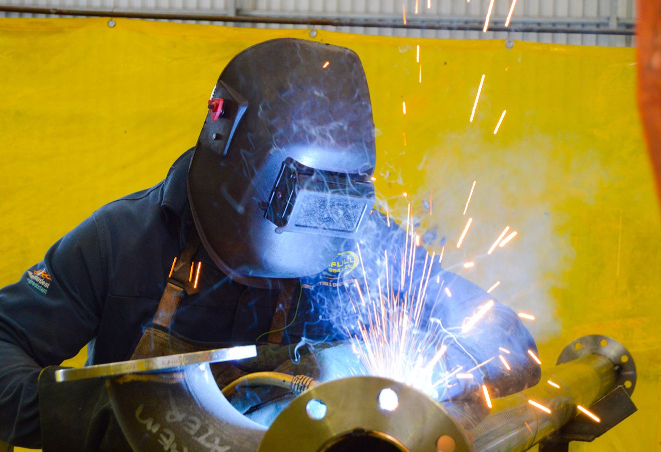 A person in blue jumpsuit and black helmet cutting a metal