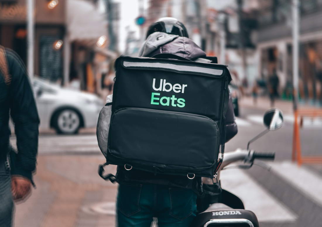 A man on a motorcycle with Uber Eats black delivery bag