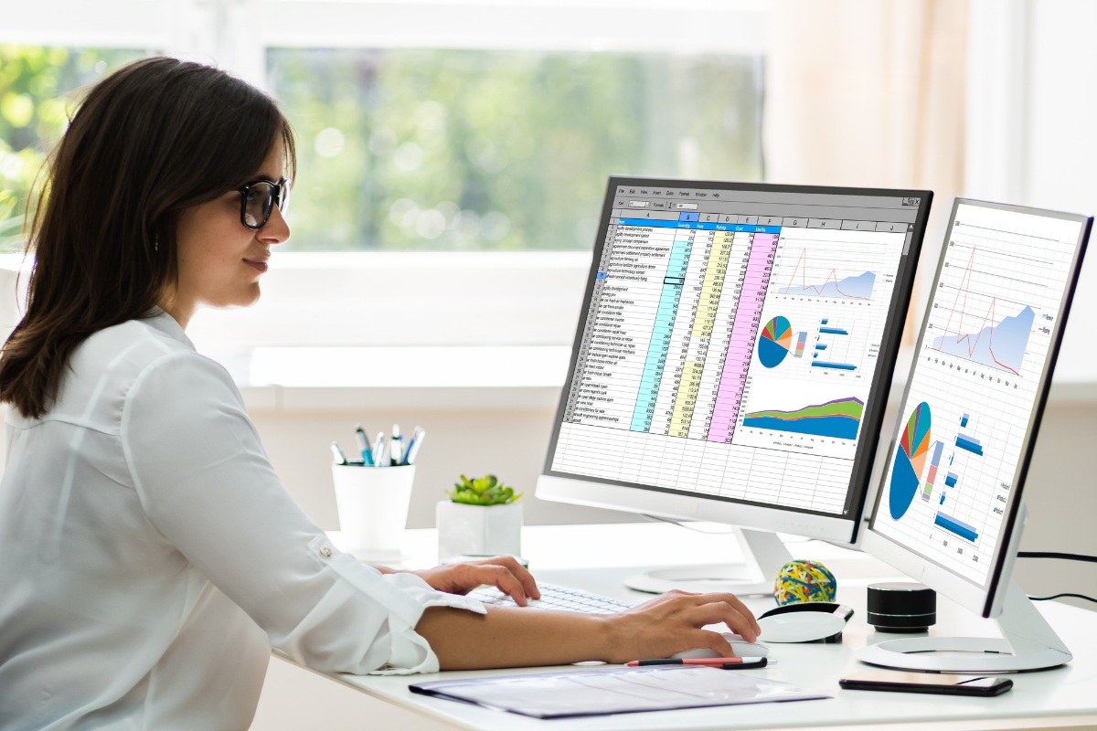 A woman in white polo long sleeves in front of two monitors with graphs