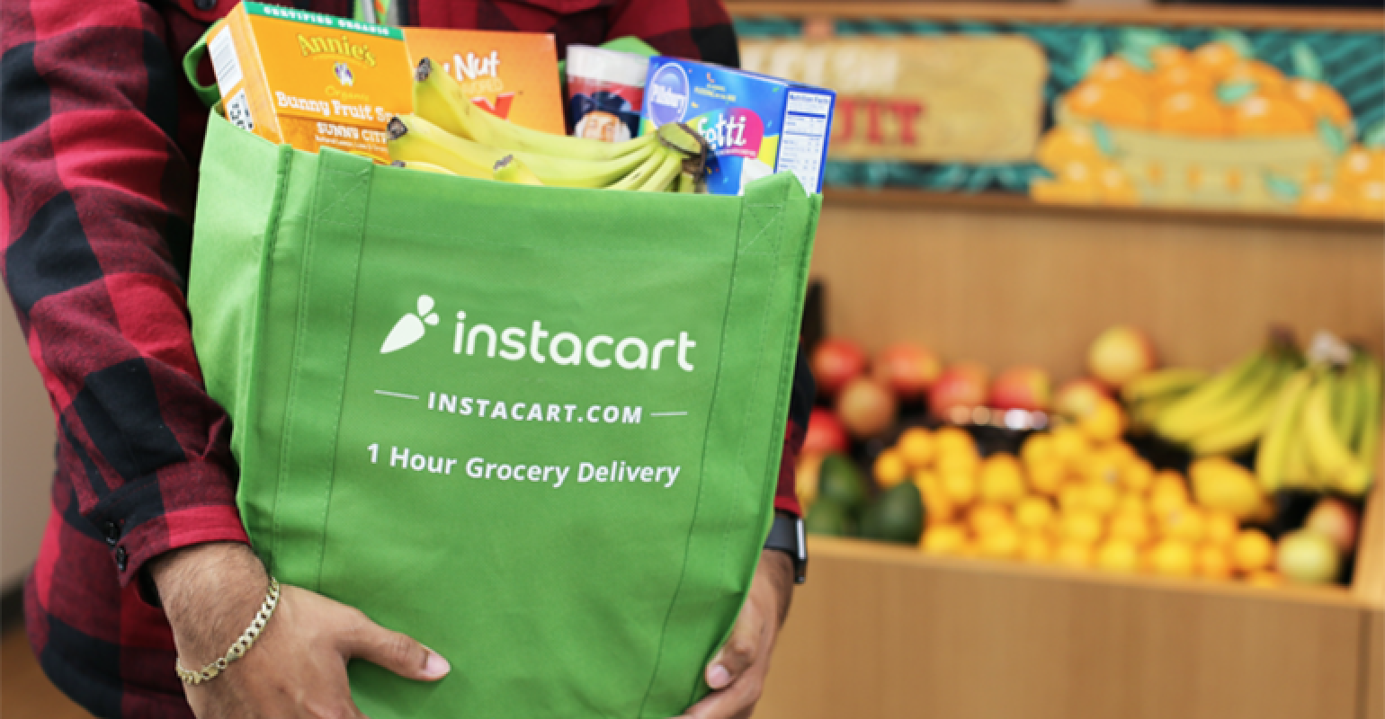 A man holding a green Instacart grocery bag with fruits beside it