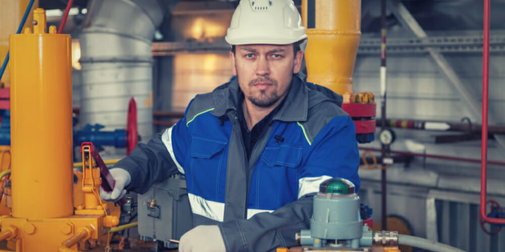 A man in blue and gray jacket with white helmet while holding a pipeline