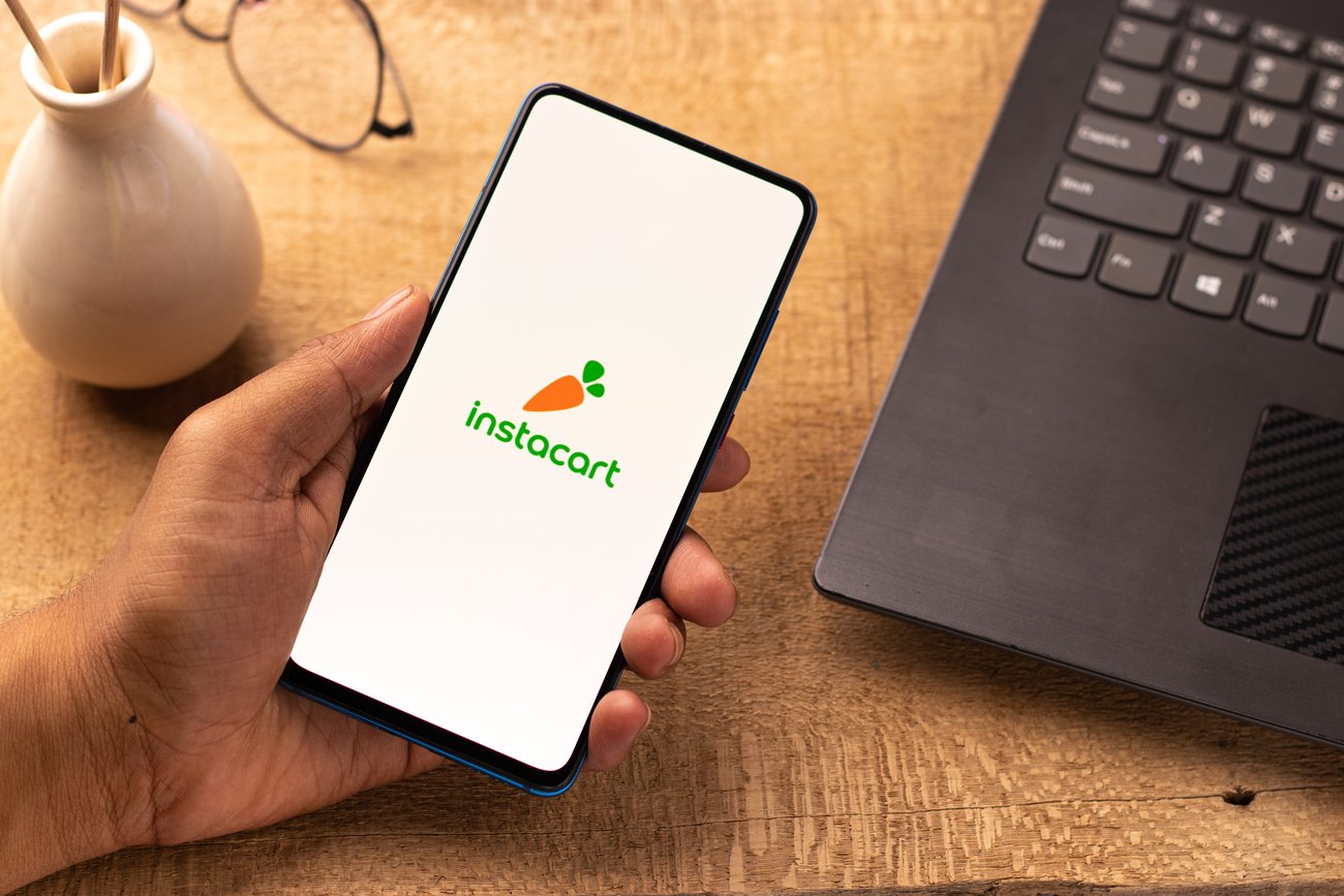 Instacart logo on a phone with laptop beside it
