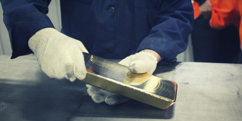 A man in blue jumpsuit holding a gold bar