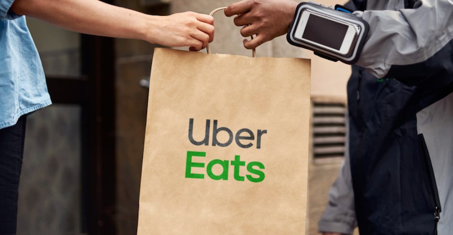A man giving an Uber Eats paper bag to a woman