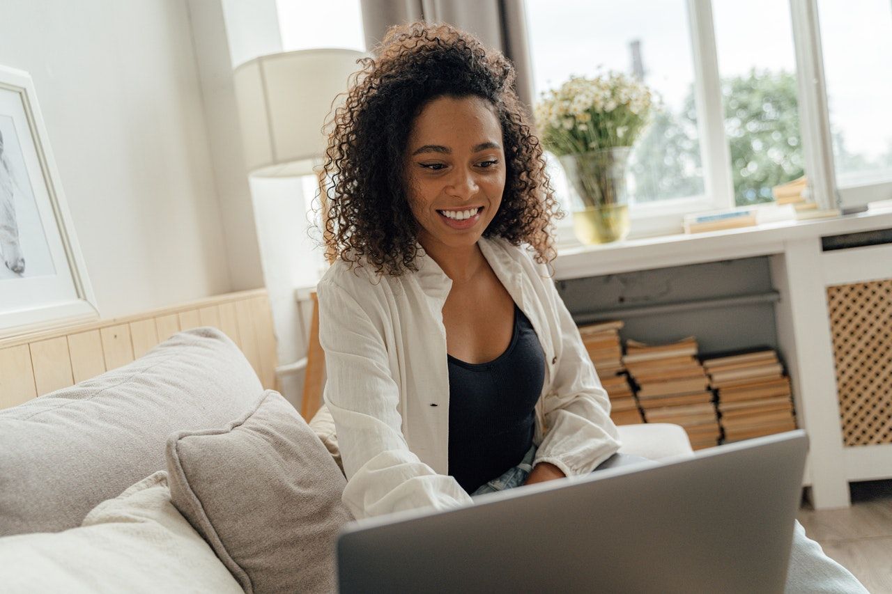 A woman in white long sleeves smiling while looking at the laptop in front of her