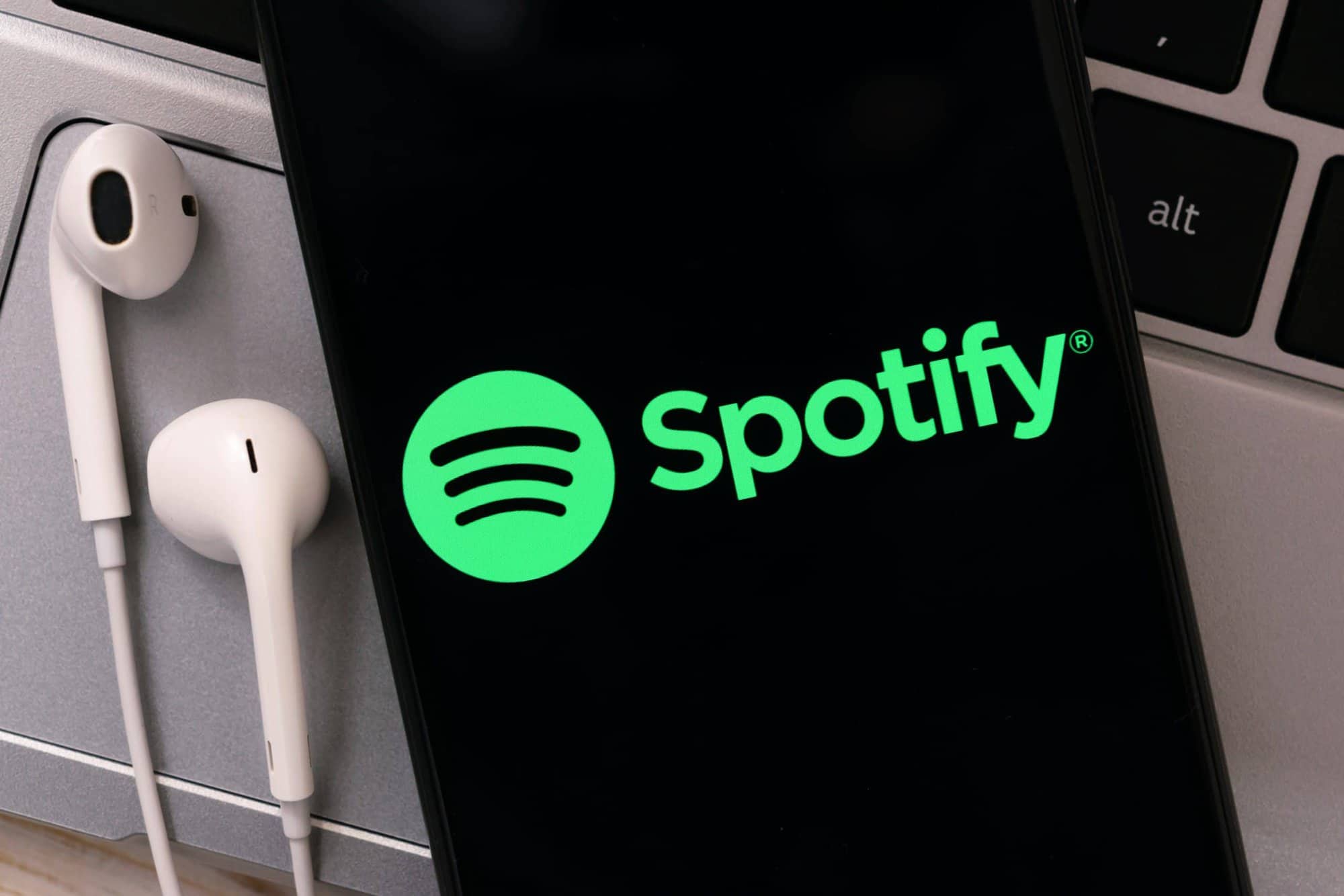 Spotify logo on a phone with earphones on top of a laptop